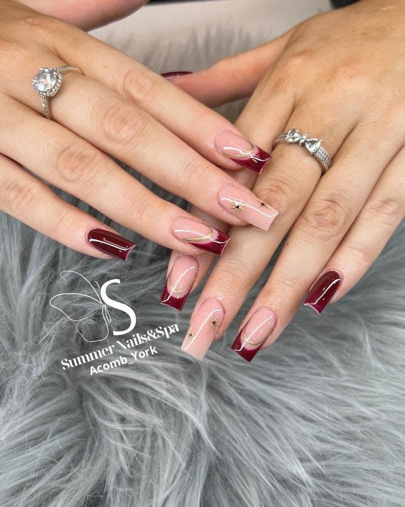 Burgundy French tips on a nude base with gem accents